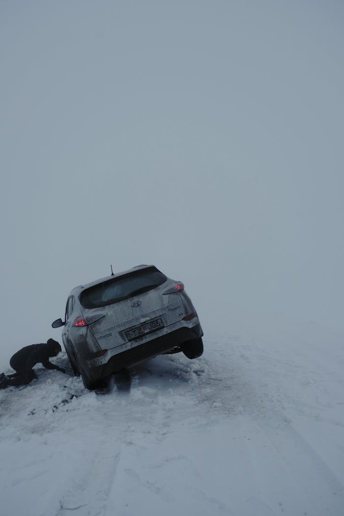 A person trying to rescue a car stuck in snow on a cold winter day.